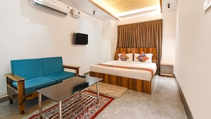 A hotel room with a bed, a blue sofa, a small table, an air conditioner, a TV, and a ceiling fan. - Fabhotel Welcome Premium (Bhubaneshwar)