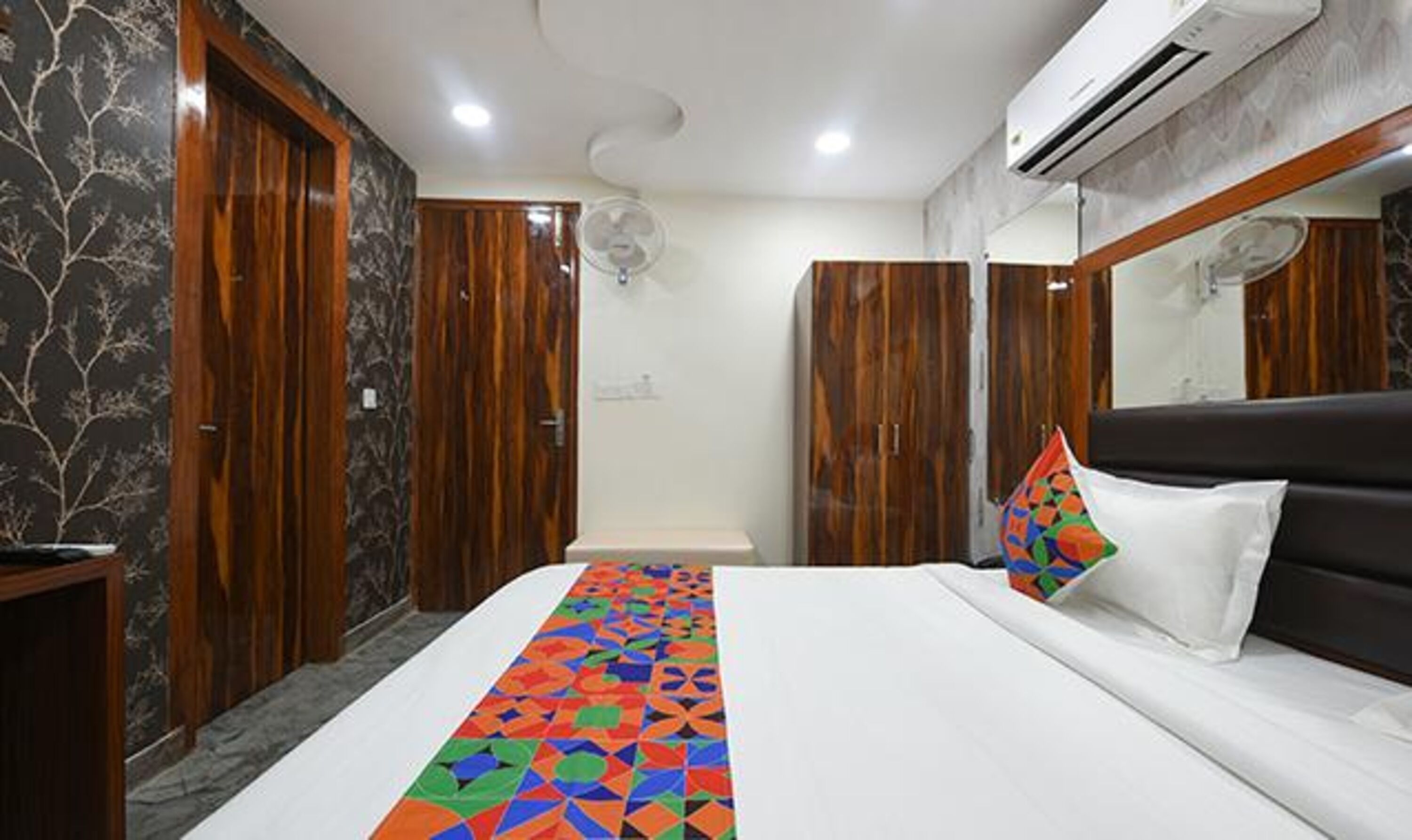 A hotel room with a bed, a dresser, an air conditioner, and a mirror.