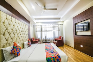 A hotel room with a tufted headboard, a bed with colorful pillows, a ceiling fan, a TV mounted on the wall, and a window with curtains. - Fabhotel Prime Neelam (Manali)