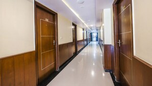Un lungo e stretto corridoio con porte in legno su entrambi i lati, targhette numerate per le stanze e pavimento piastrellato.