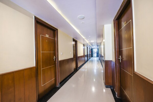 Un pasillo largo y estrecho con puertas de madera a ambos lados, carteles de números de habitación y suelo de baldosas.