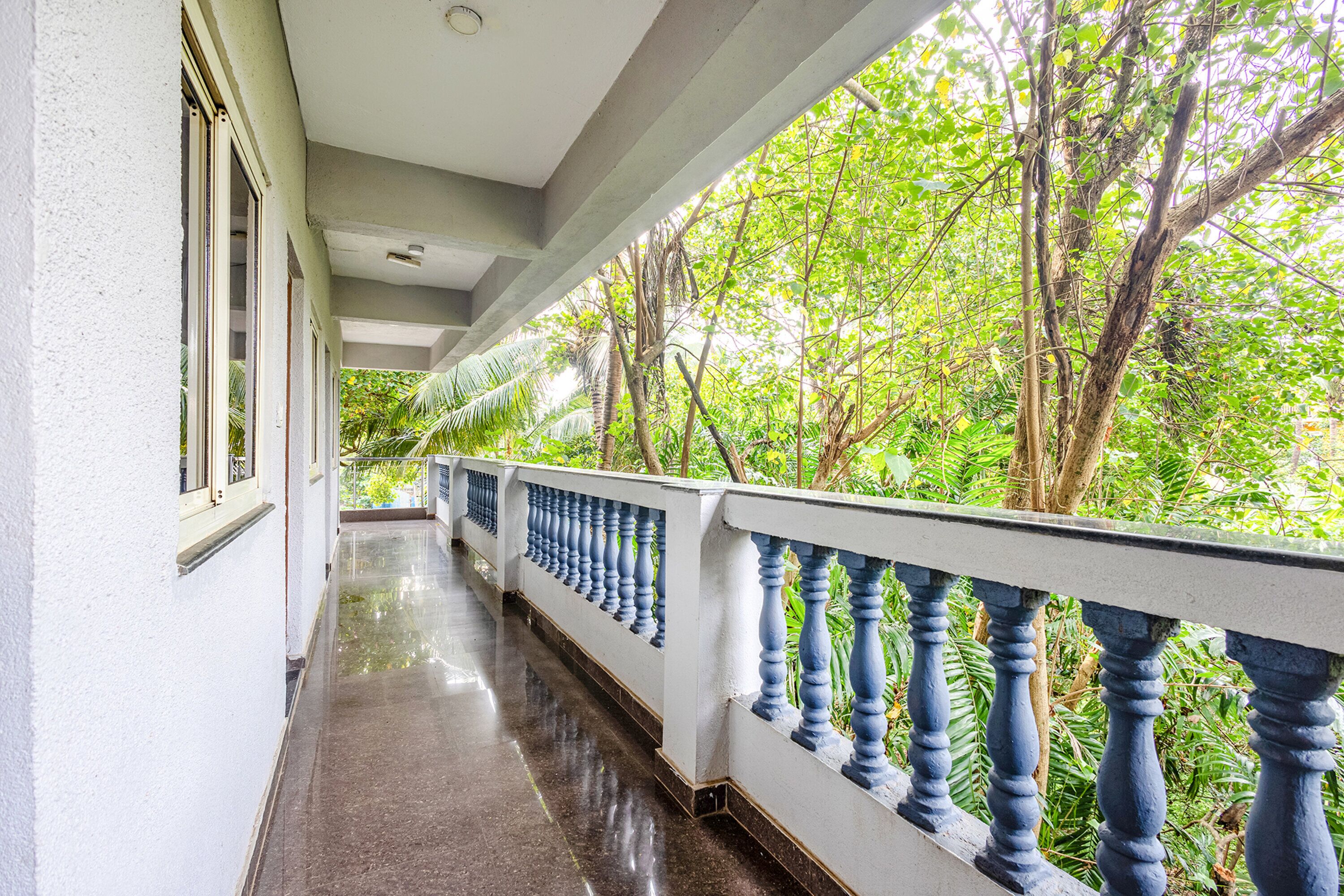 A covered corridor with a white railing and a view of lush greenery.