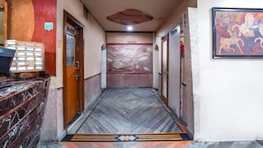 Un couloir d’hôtel avec un sol en marbre, un comptoir d’accueil, une fresque murale et une œuvre d’art encadrée.
