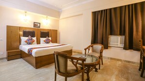 A hotel room with a bed, two chairs, a small table, a window with curtains, and a ceiling fan. - FabHotel Comfort Residency II (Gurugram)