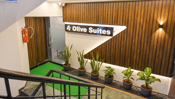 A hotel reception area with a sign for 'Olive Suites'. There are potted plants and a fire extinguisher visible. - FabHotel Olive Suite (Pune)