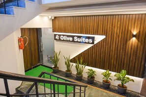 A hotel reception area with a sign for 'Olive Suites'. There are potted plants and a fire extinguisher visible. - FabHotel Olive Suite - Near Airforce Get (Pune)