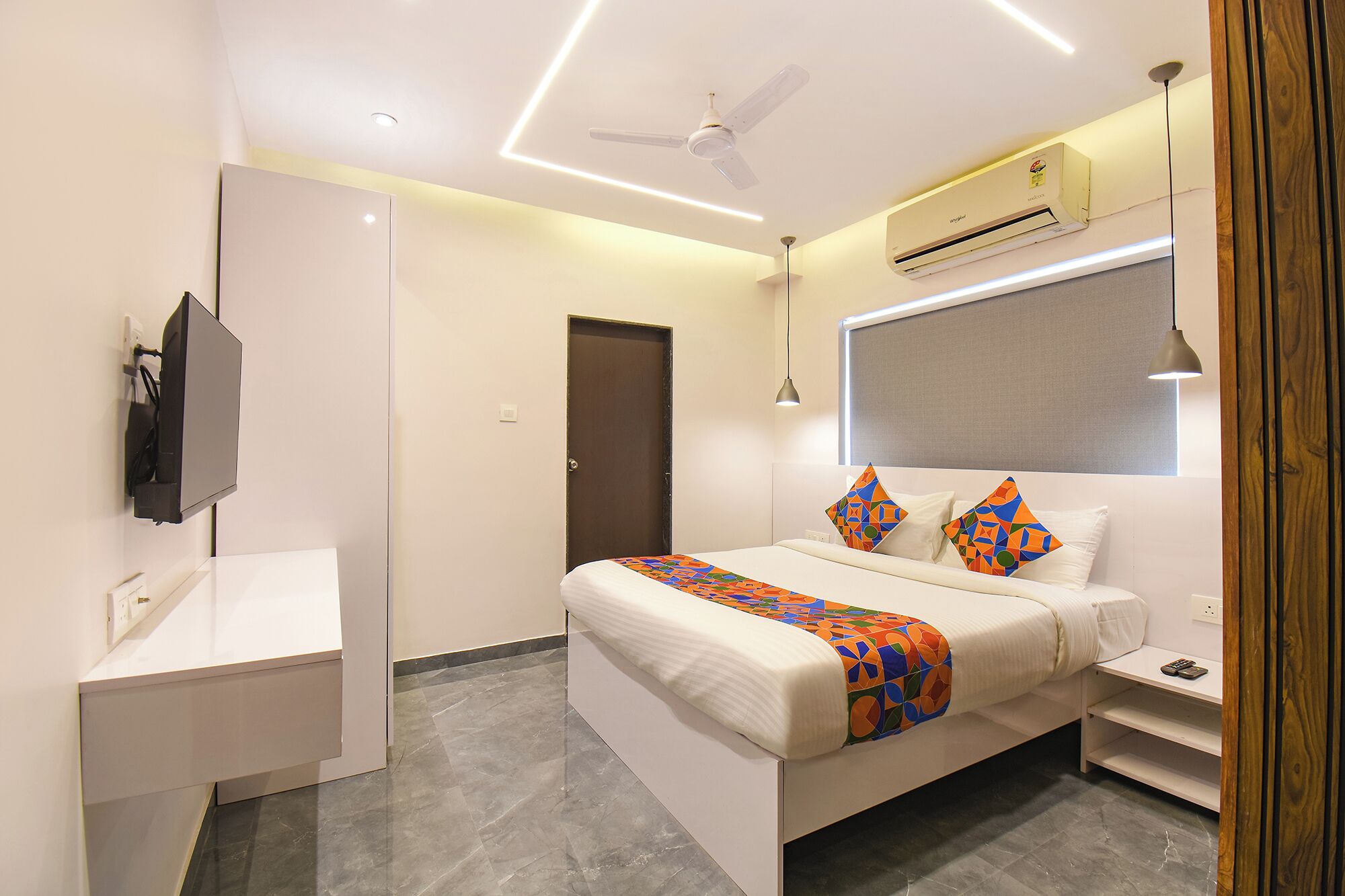 A modern hotel room with a bed, bedside table, and a TV mounted on the wall.