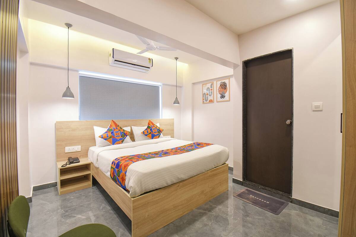 A modern bedroom with a wooden bed, a bedside table, an air conditioning unit, and a door to the bathroom.