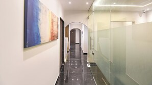 A modern hallway with a marble floor, glass walls, and a large abstract painting on the left. - FabHotel Olive Suite (Pune)