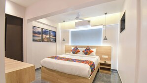 A modern hotel room with a wooden bed, a nightstand, a desk, and a large window with blinds. - FabHotel Olive Suite (Pune)