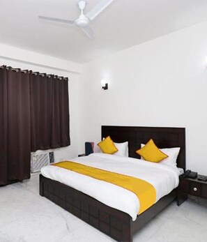 A bedroom with a bed, a nightstand, a ceiling fan, and a window with curtains. - Fabhotel The Primero (Gurugram)