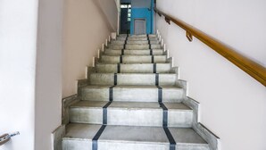 Een trap met betonnen treden en zwarte randafwerking, die leidt naar een ruimte met een blauwe muur en een deur.
