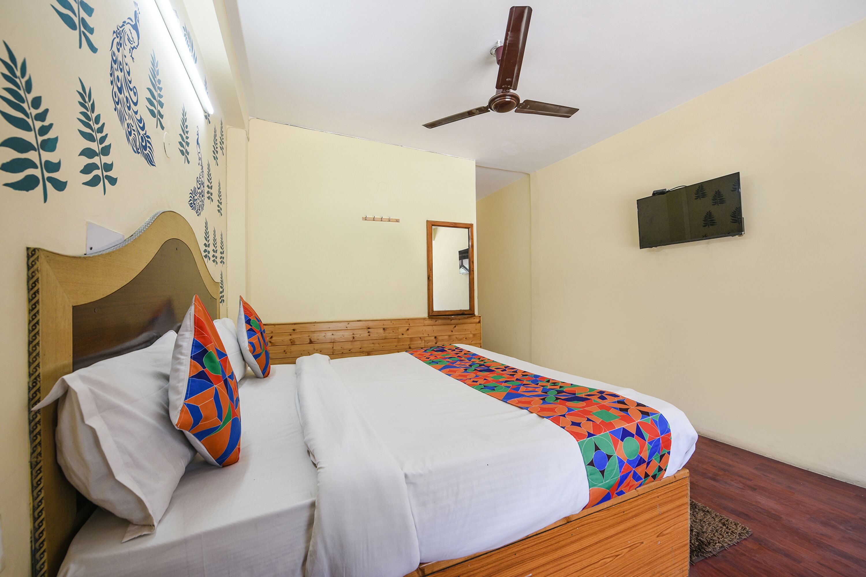 A bedroom with a wooden bed, white bedding, a ceiling fan, a mirror, and decorative wall art.