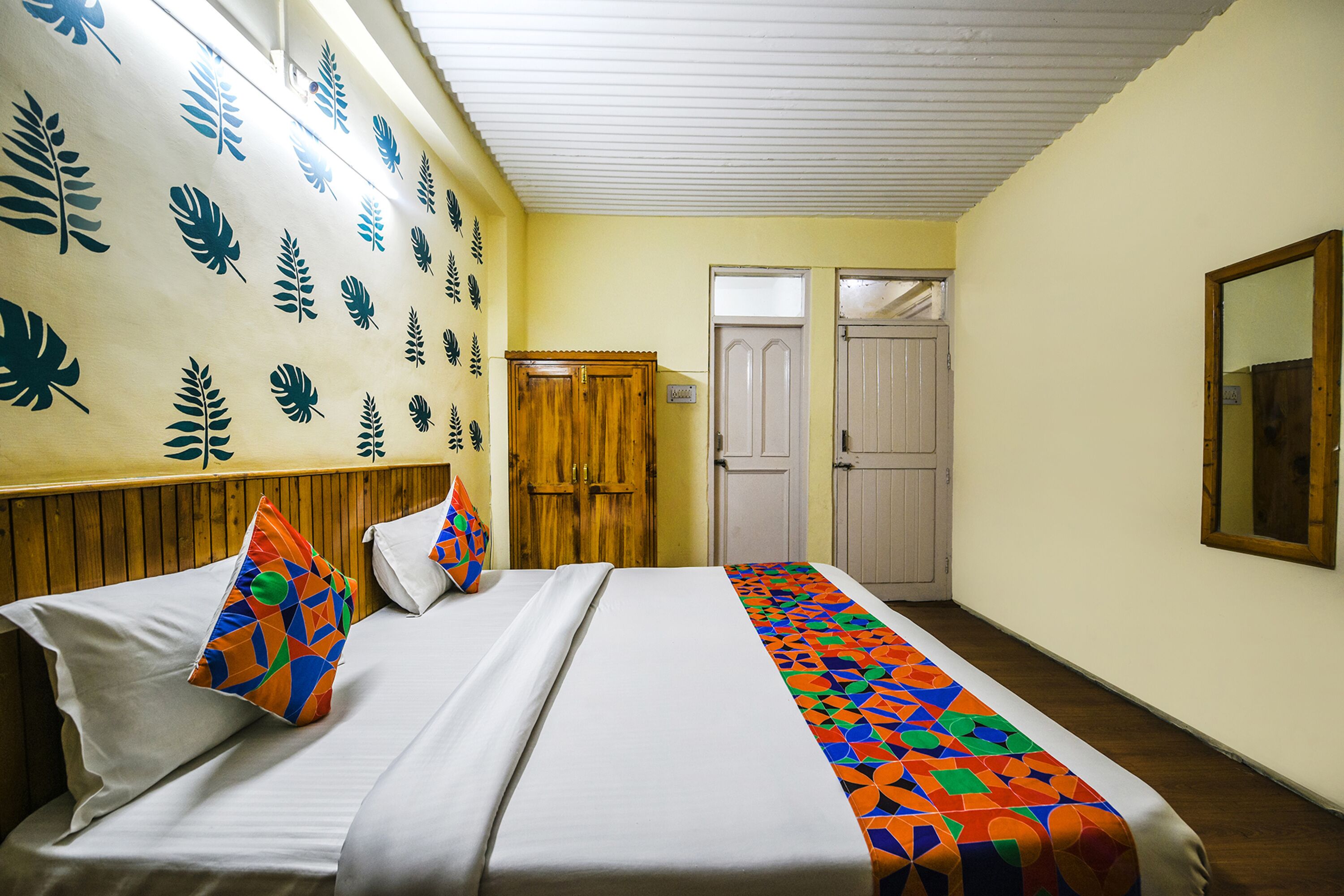 A hotel room with a bed, a wooden wardrobe, a door, and a mirror on the wall.