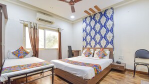 Une chambre d’hôtel avec deux lits, un ventilateur de plafond, un climatiseur, une fenêtre avec des rideaux, un mur décoré et un plancher en bois.