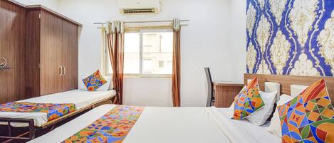 A hotel room with two single beds, a wooden wardrobe, a desk, and a window with curtains.