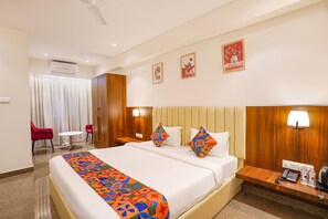 A hotel room with a large bed, two bedside tables, a desk, a chair, and a small table. - FabHotel Trubell Electronic City (Anekal)