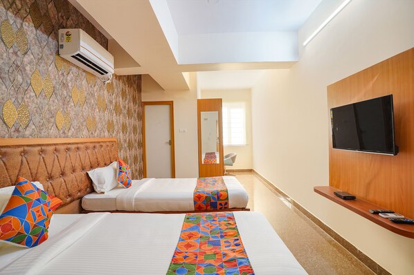 A hotel room with two beds, a TV, and an air conditioning unit.