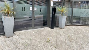 Ein modernes Gebäude mit großen Glasfenstern, auf denen "Broadway Residences" steht. Vor dem Eingang befinden sich zwei Zimmerpflanzen.