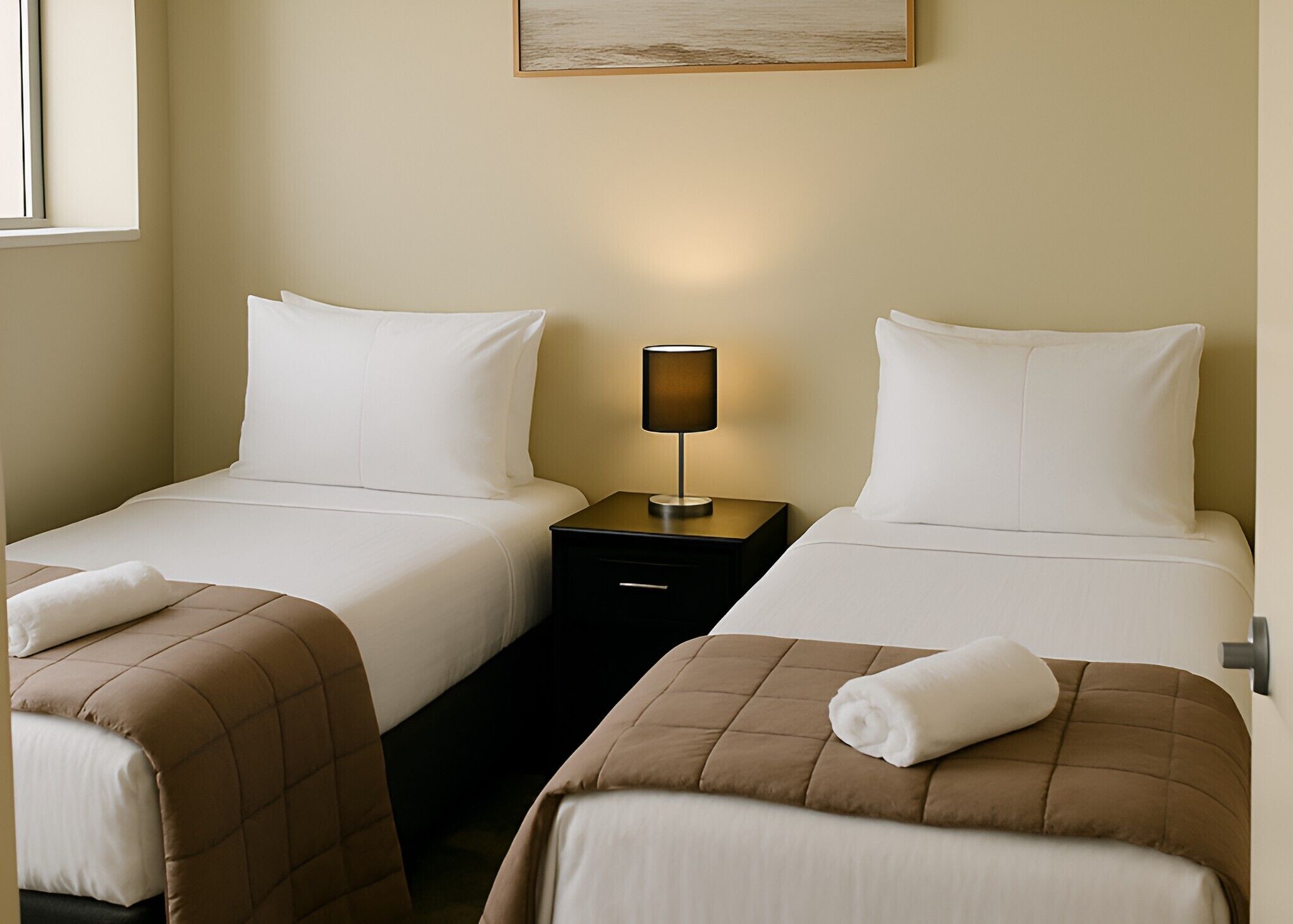 A hotel room with two beds, a nightstand with a lamp, and a painting on the wall.