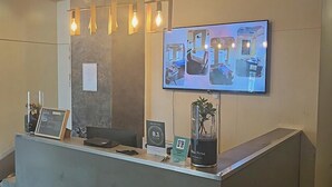 A hotel reception desk with a modern design, a mounted television displaying room images, and a sign indicating the hotel's name. - The Post Hotel (Porirua)