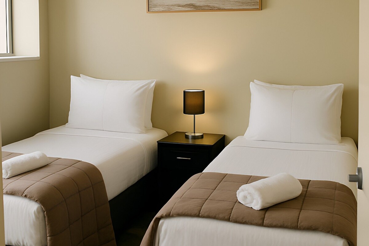 A hotel room with two beds, a nightstand with a lamp, and a painting on the wall.