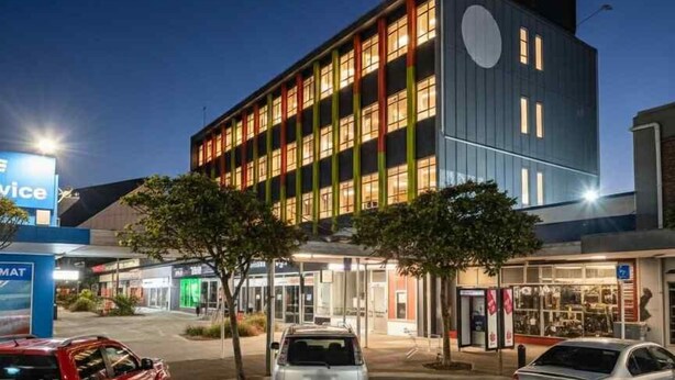 A modern building with a large circular window, a parking lot with a handicapped parking space, and a sign for 'Mice' visible in the foreground. - The Post Hotel (Porirua)