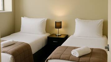 A hotel room with two single beds, a nightstand with a lamp, and a painting on the wall.