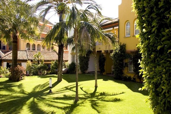 A courtyard with palm trees, a well-maintained lawn, and a yellow building with arched windows. - Hotel Soho Boutique Vistahermosa (El Puerto de Santa Maria)