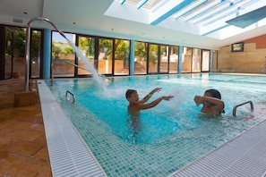 En indendørs swimmingpool med glasvægge, flisegulv og en vandfontæne.