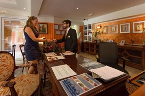 A reception area with a wooden reception desk, framed pictures on the wall, and a large window. - Hotel Soho Boutique Vistahermosa (El Puerto de Santa Maria)
