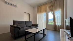 En moderne stue med sofa, sofabord, fjernsyn og et vindue med gardiner.