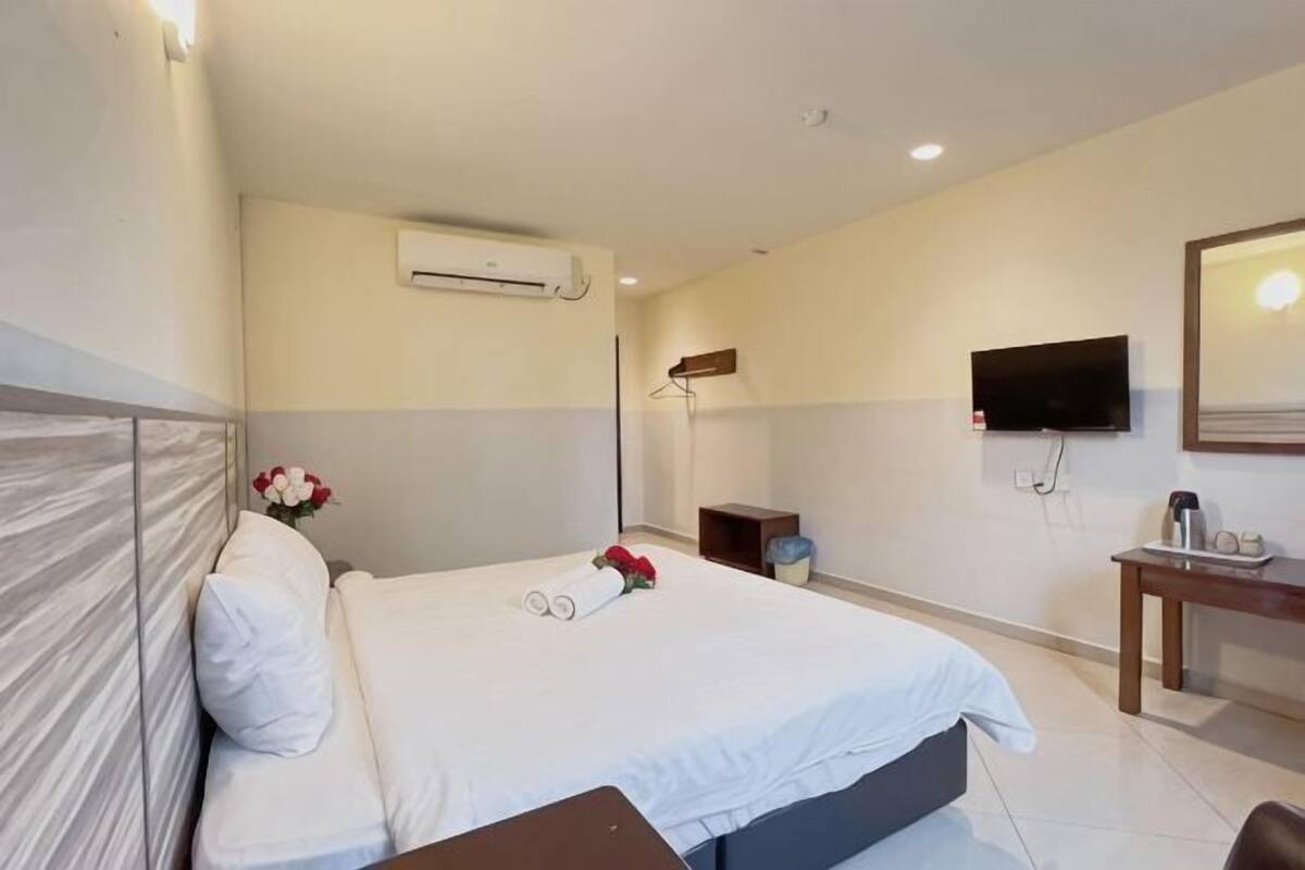 Habitación de hotel con cama, televisor de pantalla plana, mesita de noche, equipo de aire acondicionado y espejo.