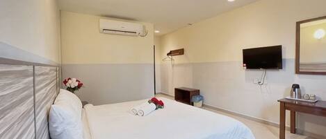 A hotel room with a bed, a flat-screen TV, a bedside table, an air conditioning unit, and a mirror.