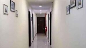 Un pasillo con puertas a ambos lados, un extintor en la pared derecha y cuadros en la pared izquierda.