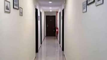 A hallway with doors on both sides, a fire extinguisher on the right wall, and framed pictures on the left wall.