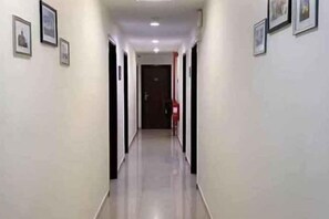 Un pasillo con puertas a ambos lados, un extintor en la pared derecha y cuadros en la pared izquierda.