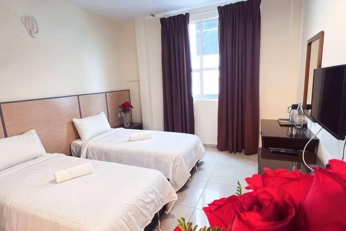 Una habitación de hotel con dos camas, televisor, escritorio y ventana con cortinas.