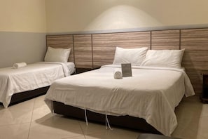 A hotel room with two single beds and one double bed, all with white bedding.