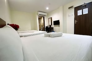 A hotel room with two beds, a desk, a chair, a TV, and a door.