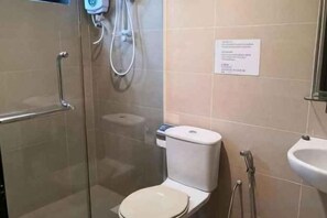 Un baño con inodoro, lavamanos y zona de ducha con mampara de vidrio.