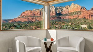 A balcony with two white leather chairs and a small round table with two mugs. The balcony overlooks a scenic view of red rock formations and a green valley. - Signature Uptown Retreat with Epic Views & Hot Tub (Sedona)
