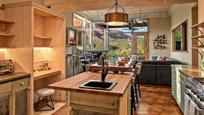A modern kitchen with wooden cabinetry, a central island with a sink, and a view of a mountainous landscape through large windows. - Signature Uptown Retreat with Epic Views & Hot Tub (Sedona)