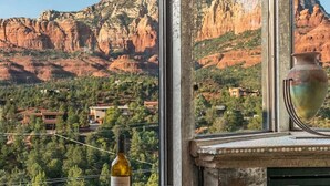 A round table with a bottle of wine, a glass, and playing cards, set against a mountain view through large windows. - Signature Uptown Retreat with Epic Views & Hot Tub (Sedona)