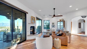 A spacious living area with a large glass sliding door leading to an outdoor patio, a fireplace, a ceiling fan, and a cozy seating arrangement. - Casa Milagro - A designer desert retreat! (Tucson)