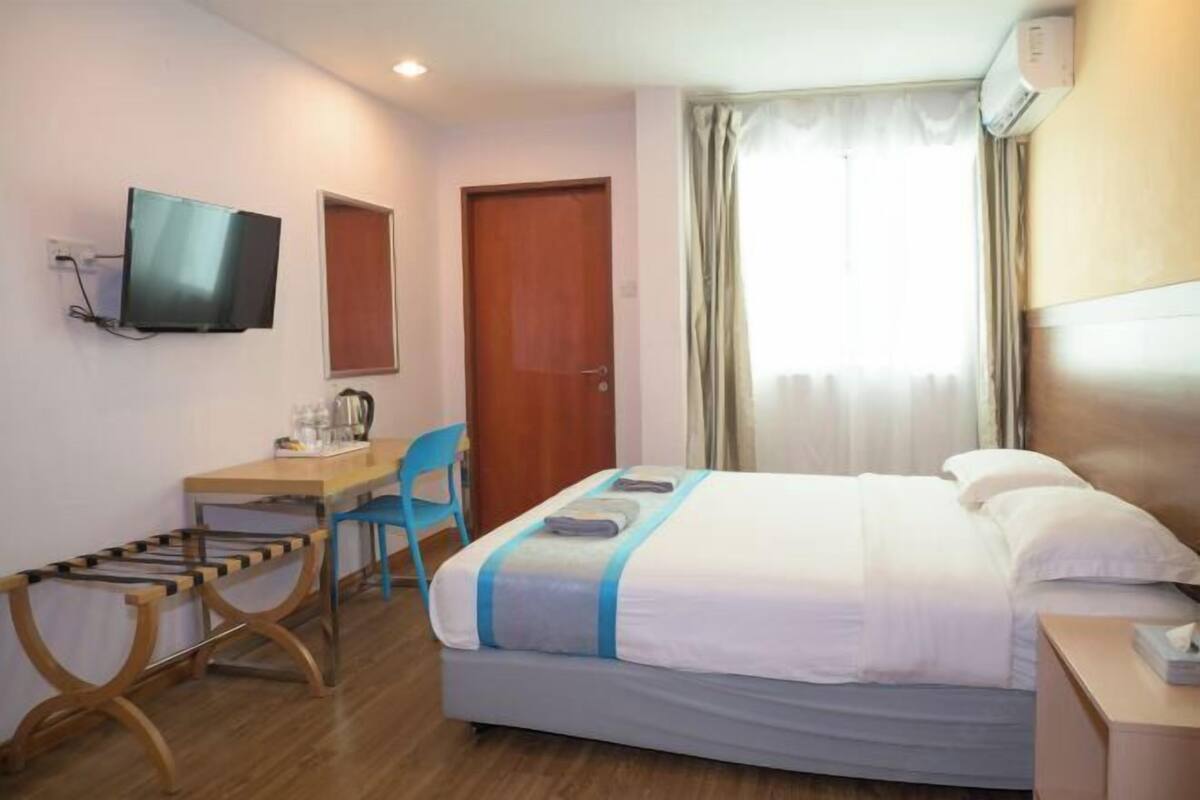 A hotel room with a bed, a desk with a chair, a television, and a window with curtains.