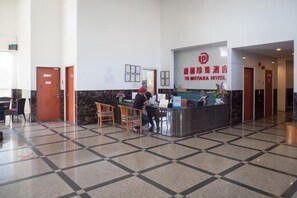 A hotel reception area with a check-in counter, chairs, and a tiled floor.