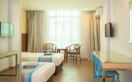 Una habitación de hotel con dos camas, un escritorio, sillas, un televisor y una ventana con cortinas.