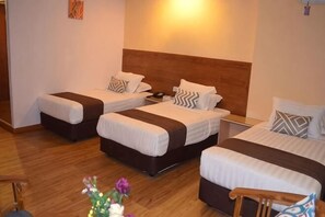 A hotel room with three beds, wooden headboard, bedside tables, and a nightstand.