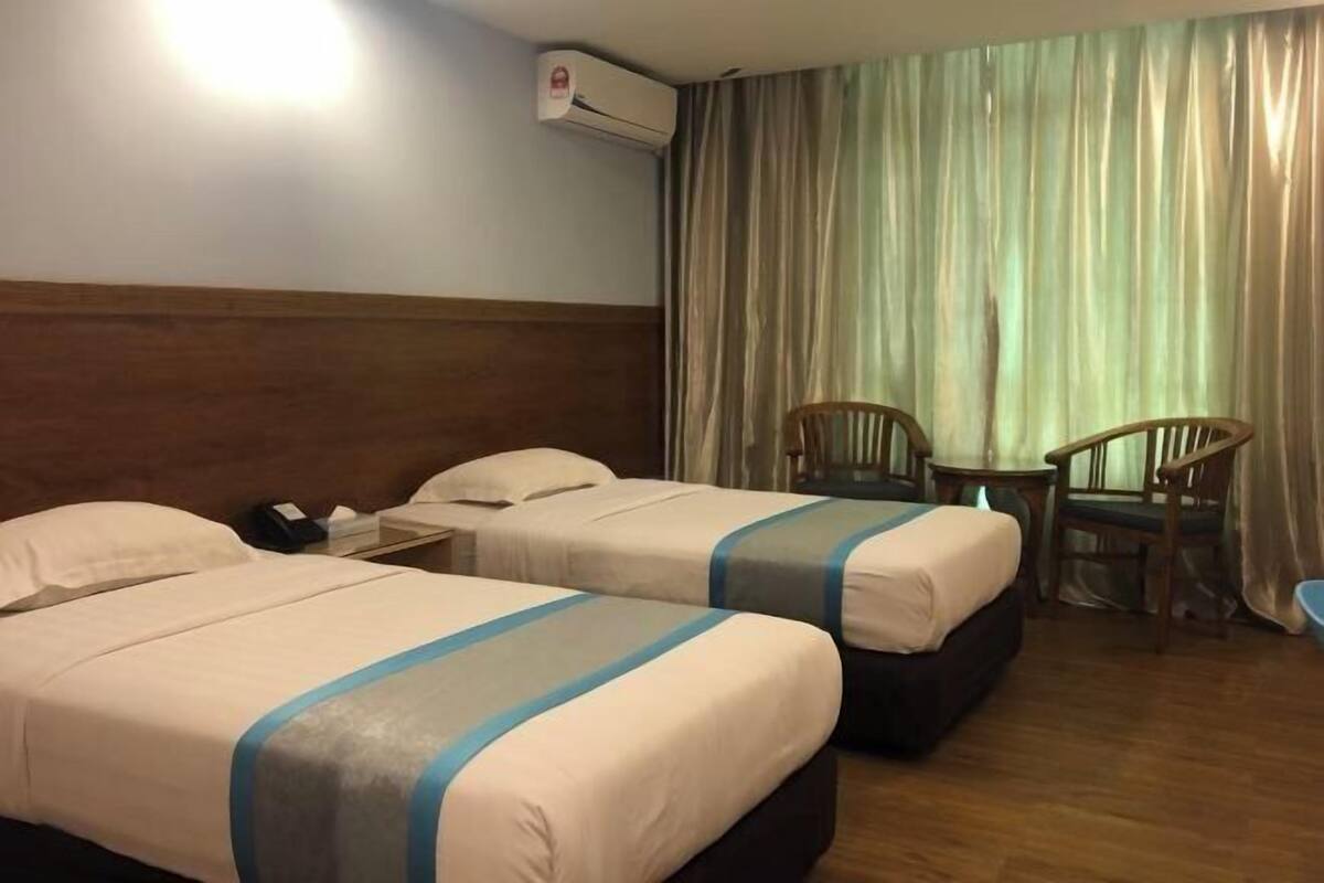A hotel room with two beds, a desk, a chair, and an air conditioning unit.